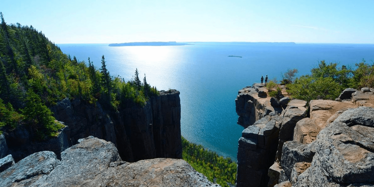 Two hikers standing on a high rock overlooking a lake