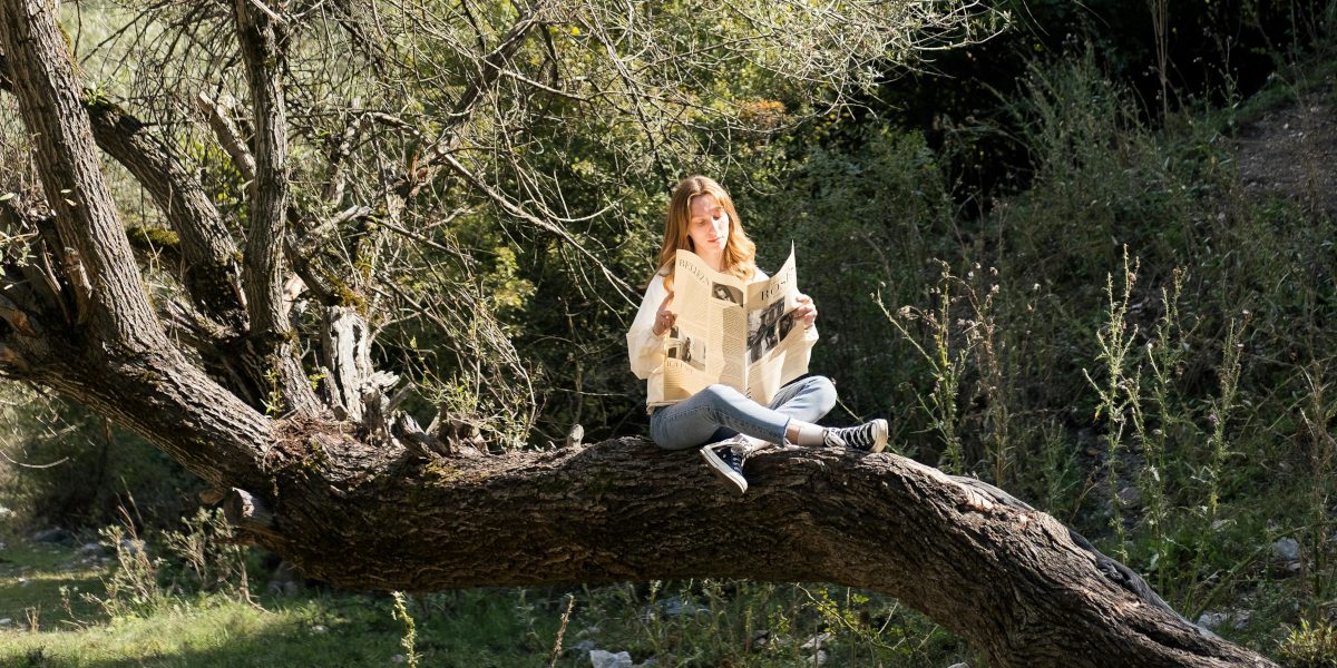 Girl sitting on a fallen tree and reading a newspaper